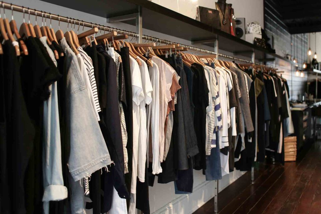 Neutral-colored clothing hangs on a store rack (Photo Credit: Pexels/Rachel Claire)
